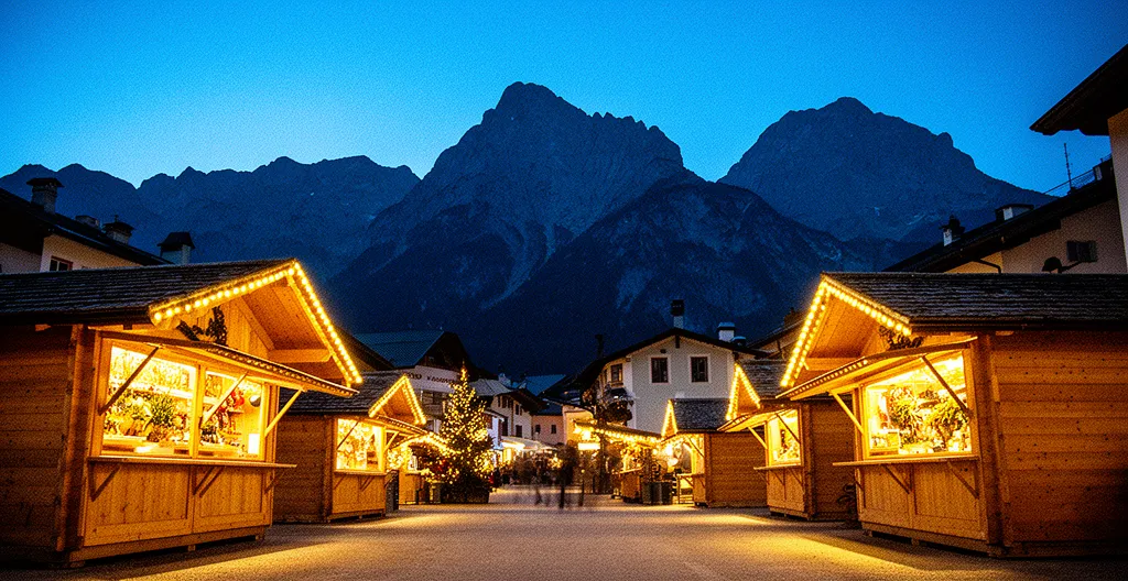 Vista panoramica dei mercatini di Natale dell'Alto Adige con casette di legno illuminate e montagne innevate sullo sfondo