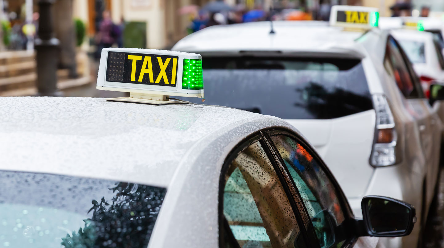 Taxi bianco parcheggiato su strada costiera di Ibiza con mare Mediterraneo e architettura tipica bianca sullo sfondo
